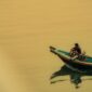 Seorang nelayan tradisional menggunakan perahu kayu memancing ikan dengan metode ramah lingkungan di perairan pesisir Indonesia saat matahari terbenam. Praktik penangkapan ikan secara tradisional ini membantu menjaga kelestarian terumbu karang serta populasi biota laut Nusantara.