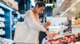 Seorang warga menggunakan tas belanja ramah lingkungan saat memilih produk lokal segar di pasar tradisional. Kebiasaan sederhana ini menjadi salah satu pilar penunjang strategi nasional dalam menekan emisi karbon dari sektor konsumsi harian.