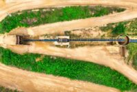 Pemandangan kontras antara kawasan hutan hijau yang asri dan bentang lahan yang rusak akibat aktivitas penambangan terbuka. Foto ini memperlihatkan besarnya jejak ekologis yang ditimbulkan oleh ekstraksi sumber daya alam demi memenuhi kebutuhan industri modern.