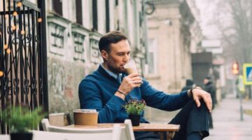 Seorang warga urban menikmati secangkir kopi pagi di tengah suasana perkotaan yang hijau, mencerminkan perpaduan rutinitas harian dan kesadaran akan gaya hidup rendah emisi karbon.