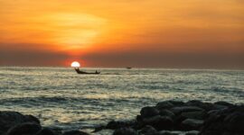 Seorang nelayan tradisional di pesisir kepulauan Indonesia bersiap melaut dengan perahu kerajinan tangan di bawah naungan cahaya matahari terbenam.