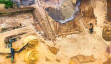 Pemandangan udara kawasan pertambangan terbuka yang mengubah bentang alam hijau menjadi celah pengerukan tanah merah untuk pemenuhan industri mineral.