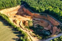 Pemandangan udara memperlihatkan bukit-bukit yang terkelupas akibat aktivitas pertambangan terbuka, memperlihatkan dampak langsung pengerukan tanah terhadap ekosistem hutan tropis Nusantara.